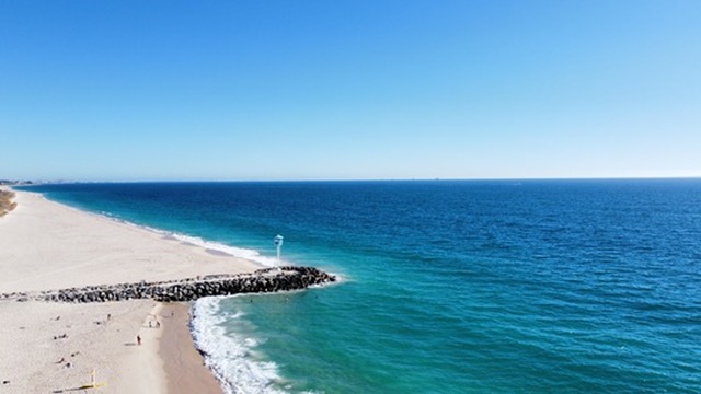A Western Australian beach with a stone groyne meeting clear blue water